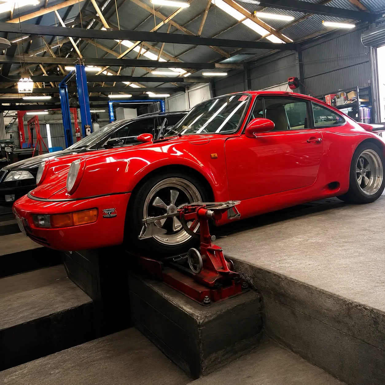 A Porsche 911 positioned over the wheel alignment pit inside the workshop